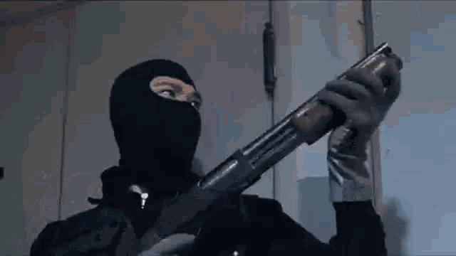 a man wearing a mask is holding a shotgun .