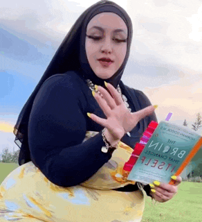 a woman in a hijab is holding a book in her hand .