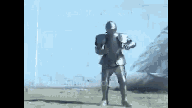 a man in a knight 's armor is standing in a field holding a sword .
