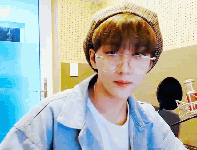 a boy wearing glasses and a hat is sitting in front of a microphone
