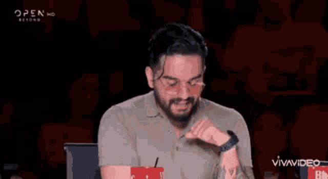 a man with a beard is sitting at a table with a cup of popcorn in front of a crowd .