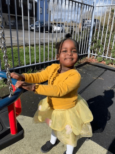 a little girl wearing a yellow sweater and a yellow tutu is sitting on a swing