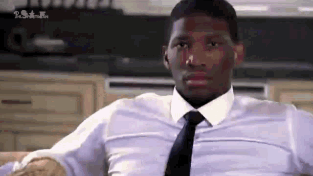 a man in a white shirt and tie is sitting on a couch in a kitchen .