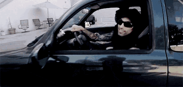 a man wearing sunglasses is driving a truck in a parking lot