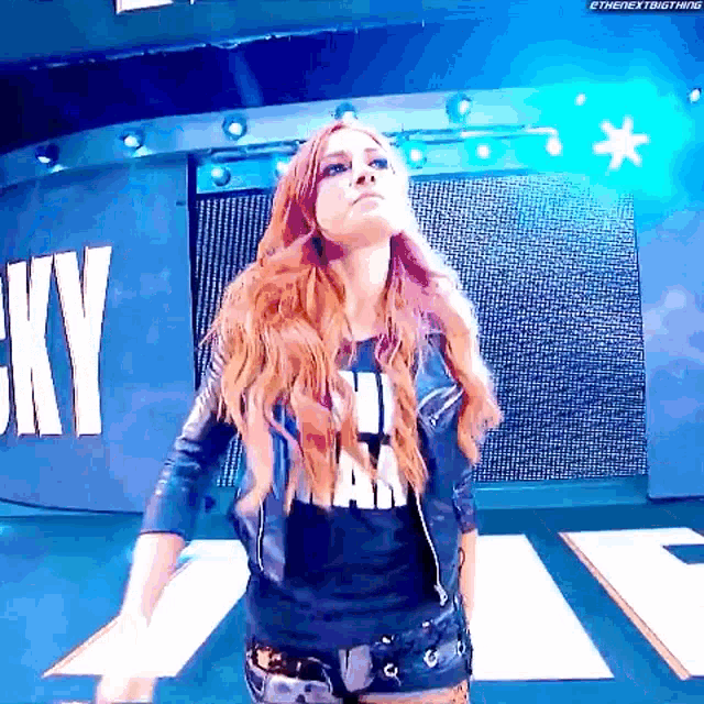a woman with red hair is standing on a stage wearing a leather jacket .
