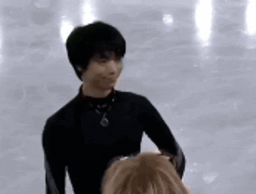 a man in a black shirt is standing on a ice rink with a woman .