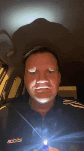 a man wearing an adidas jacket holds a flashlight in his hand