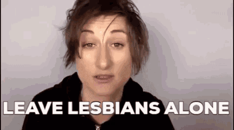 a woman is standing in front of a white wall with the words `` leave lesbians alone '' written on it .
