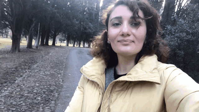 a woman in a yellow jacket takes a selfie in front of trees