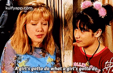 two young girls are standing next to each other and talking .