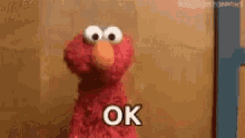 elmo from sesame street is standing in front of a wall and says `` ok '' .