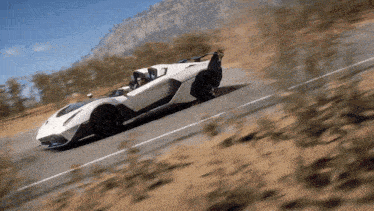 a white sports car is driving down a road with mountains in the background .