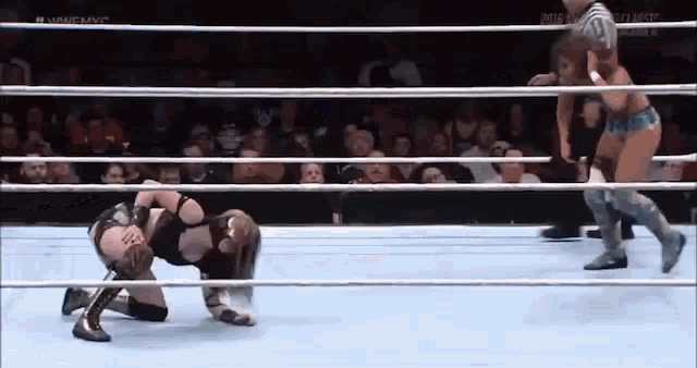 a woman is kneeling down in a wrestling ring while a referee watches .