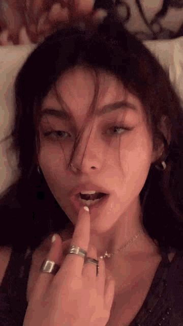 a girl is laying on a bed with her finger in her mouth and a ring on her finger .