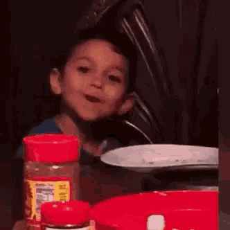 a young boy is sitting at a table with a plate and a bottle of pepper .