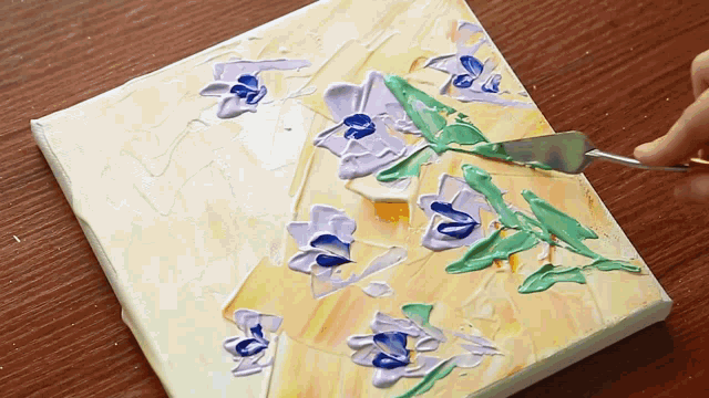 a person is using a spatula to spread paint on a painting of flowers