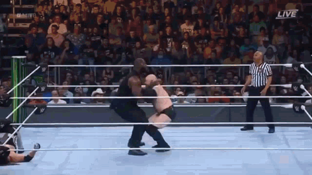 a referee is standing in a wrestling ring watching a wrestler throw another wrestler into the ring .