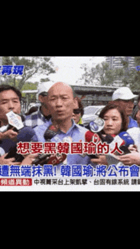 a man in a blue shirt is talking into a microphone while surrounded by other people