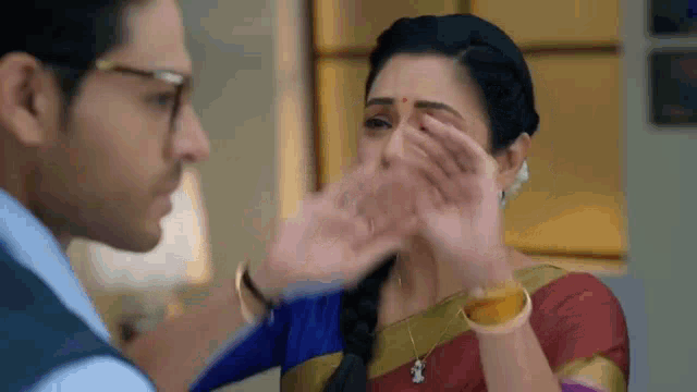 a man and a woman are standing next to each other and the woman is covering her face with her hands .