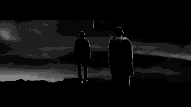 two men are standing on top of a hill looking at the mountains .