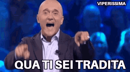 a bald man in a suit is pointing at the camera with the words qua ti sei tradita behind him