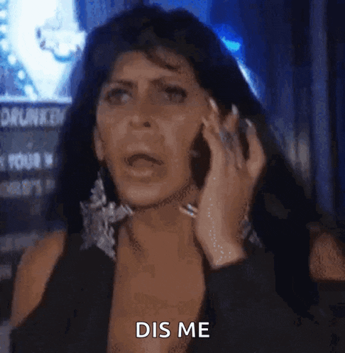 a woman in a black dress is talking on a cell phone and making a funny face .