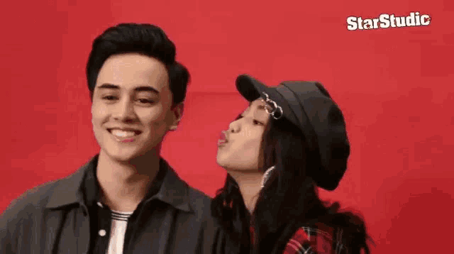 a man and a woman are posing for a picture and the woman is blowing a kiss on the man 's cheek .