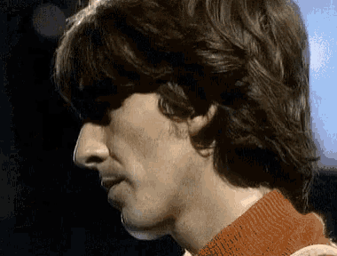 a close up of a man 's face with long hair and a red sweater