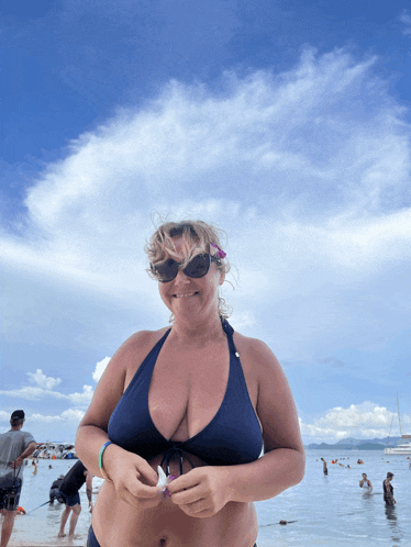 a woman in a blue bikini and sunglasses smiles at the camera