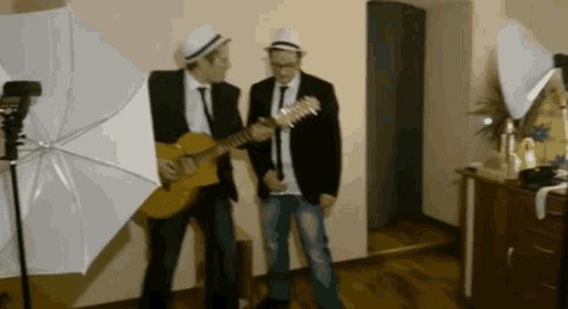two men in suits and hats are playing guitars