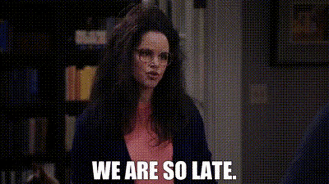 a woman wearing glasses is sitting in front of a bookshelf and saying `` we are so late . ''