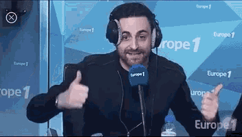 a man wearing headphones is giving a thumbs up in front of a microphone that says europe 1 on it