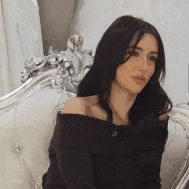 a woman in a black off the shoulder top is sitting on a couch