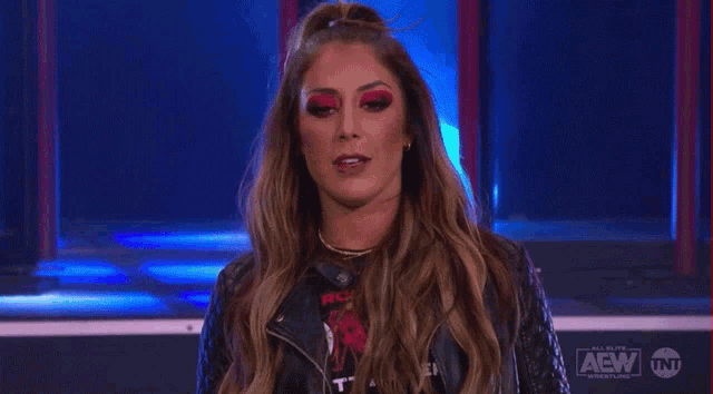 a woman in a leather jacket and red eye shadow is standing on a stage .