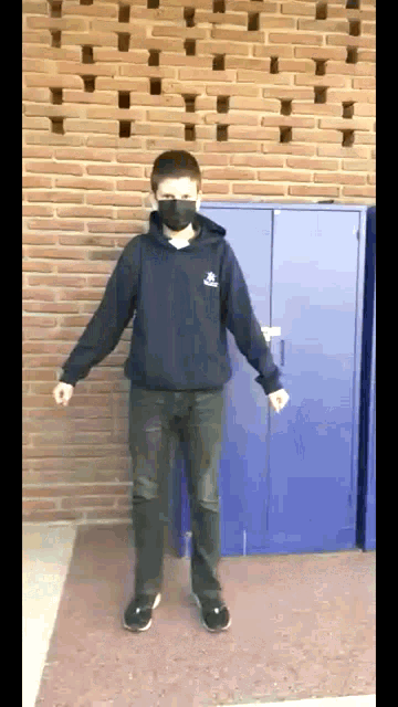a boy wearing a mask is standing in front of a brick wall and a blue cabinet