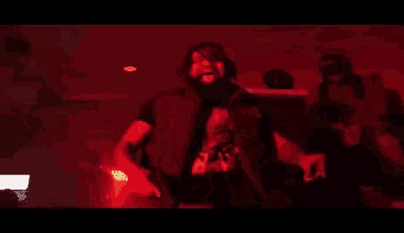 a man with a beard is standing in front of a microphone in a dark room with red lights .