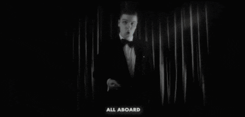 a man in a tuxedo is standing in front of a curtain with the words cancellation station written on it .