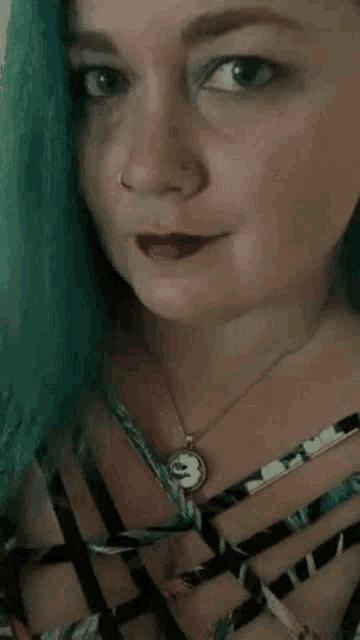 a woman with blue hair is wearing a necklace with a pendant that says s on it .