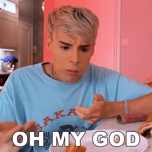 a man in a blue shirt is sitting at a table with a plate of food and the words oh my god above him .