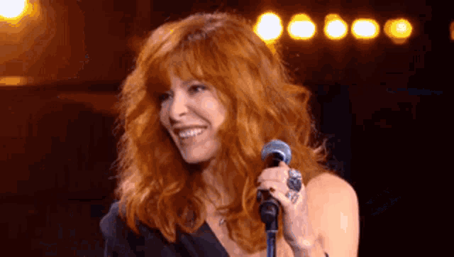 a woman with red hair is holding a microphone and smiling