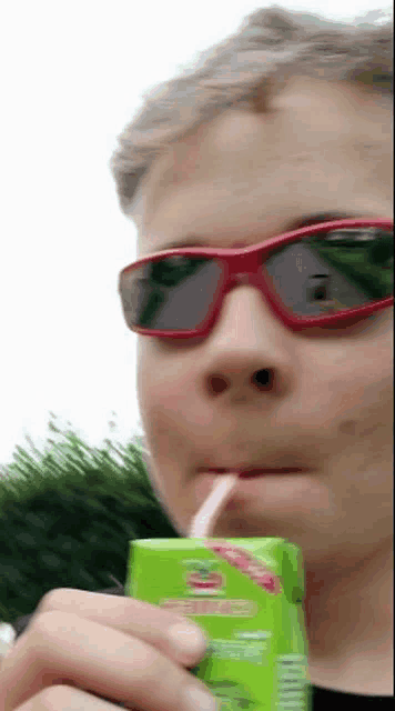 a person wearing sunglasses is drinking from a juice box