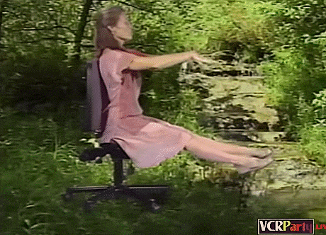 a woman in a pink dress sits on a chair in the woods