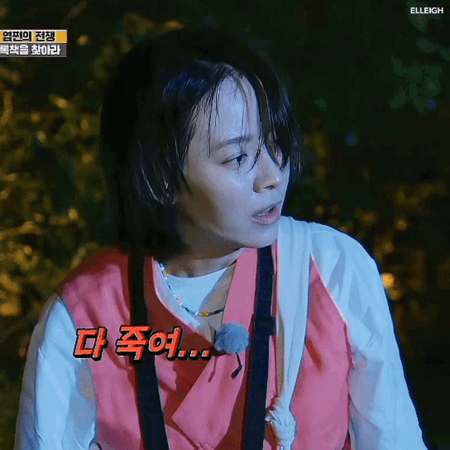 a woman in a pink vest is standing in a dark room with korean writing on the bottom right corner .
