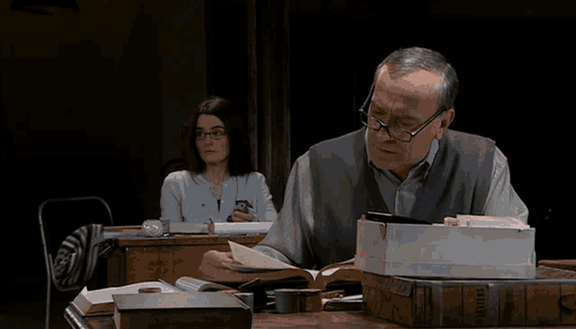 a man sits at a desk with a stack of books including one titled letters
