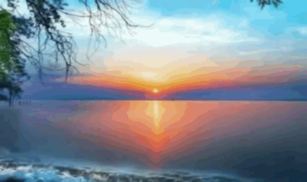 a sunset over a body of water with a tree branch in the foreground