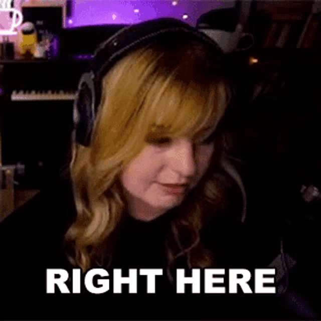 a woman wearing headphones is sitting in front of a microphone with the words `` right here '' written on her face .