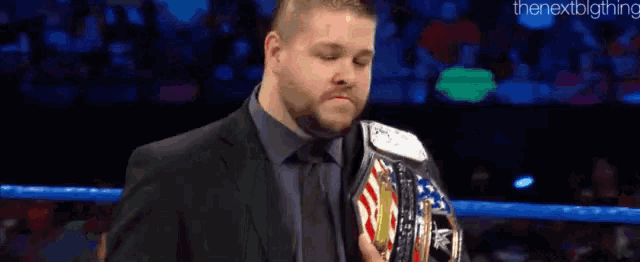 a man in a suit and tie is holding a wrestling championship belt in a ring .