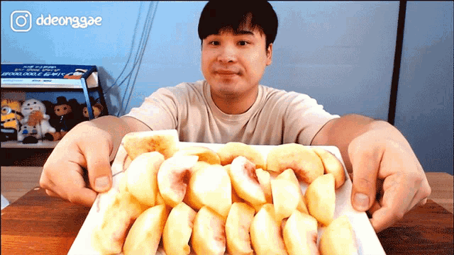 a man is holding a plate of sliced peaches in front of a box that says ddeonggae on it