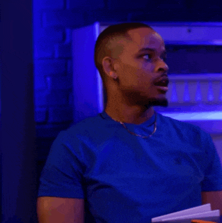 a man wearing a blue shirt and a gold chain is sitting in a dark room with blue lights .