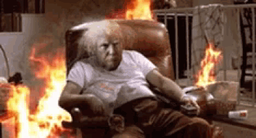 an elderly woman is sitting in a chair with fire behind her .